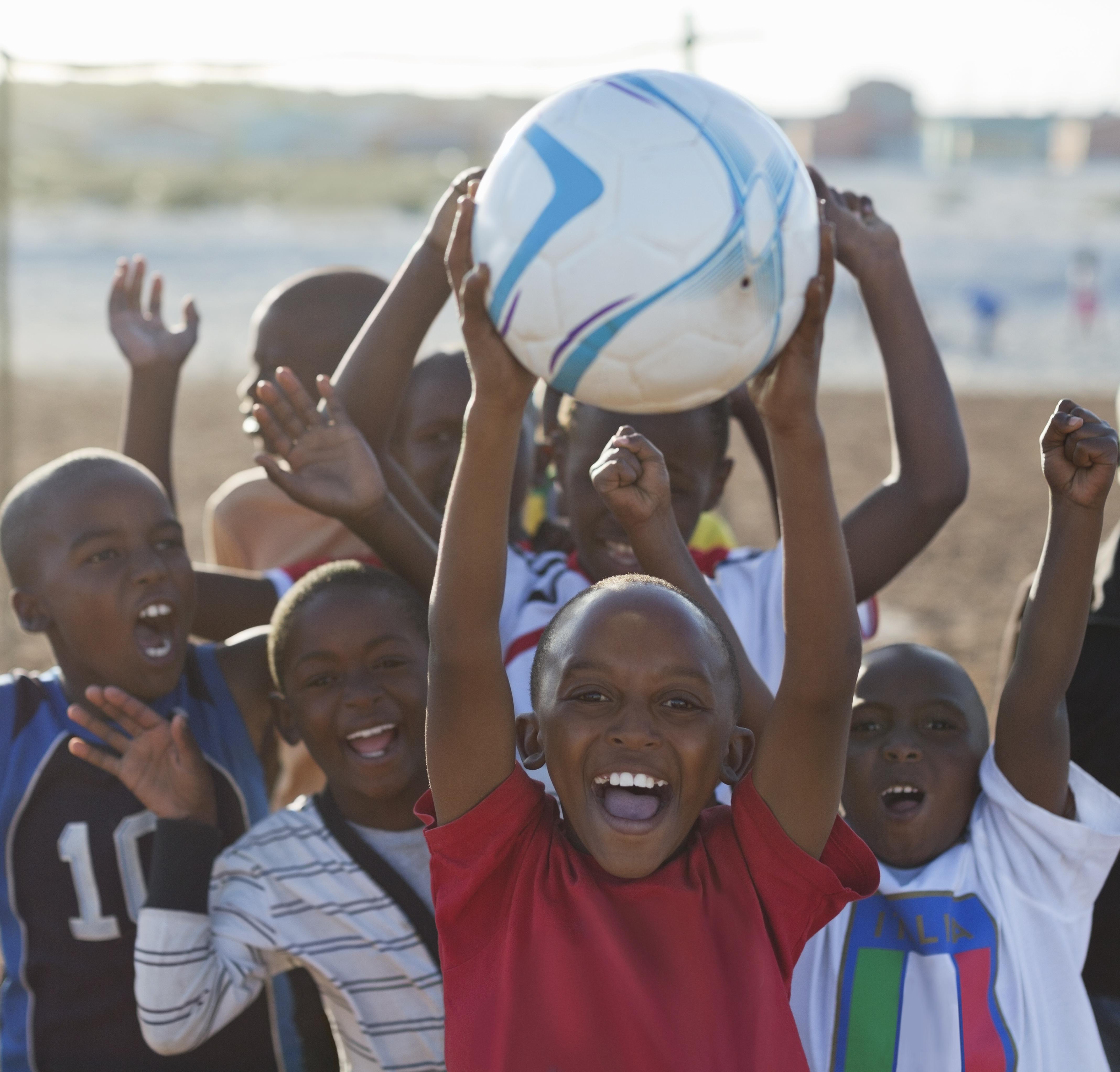 Boys playing soccer together in dirt field