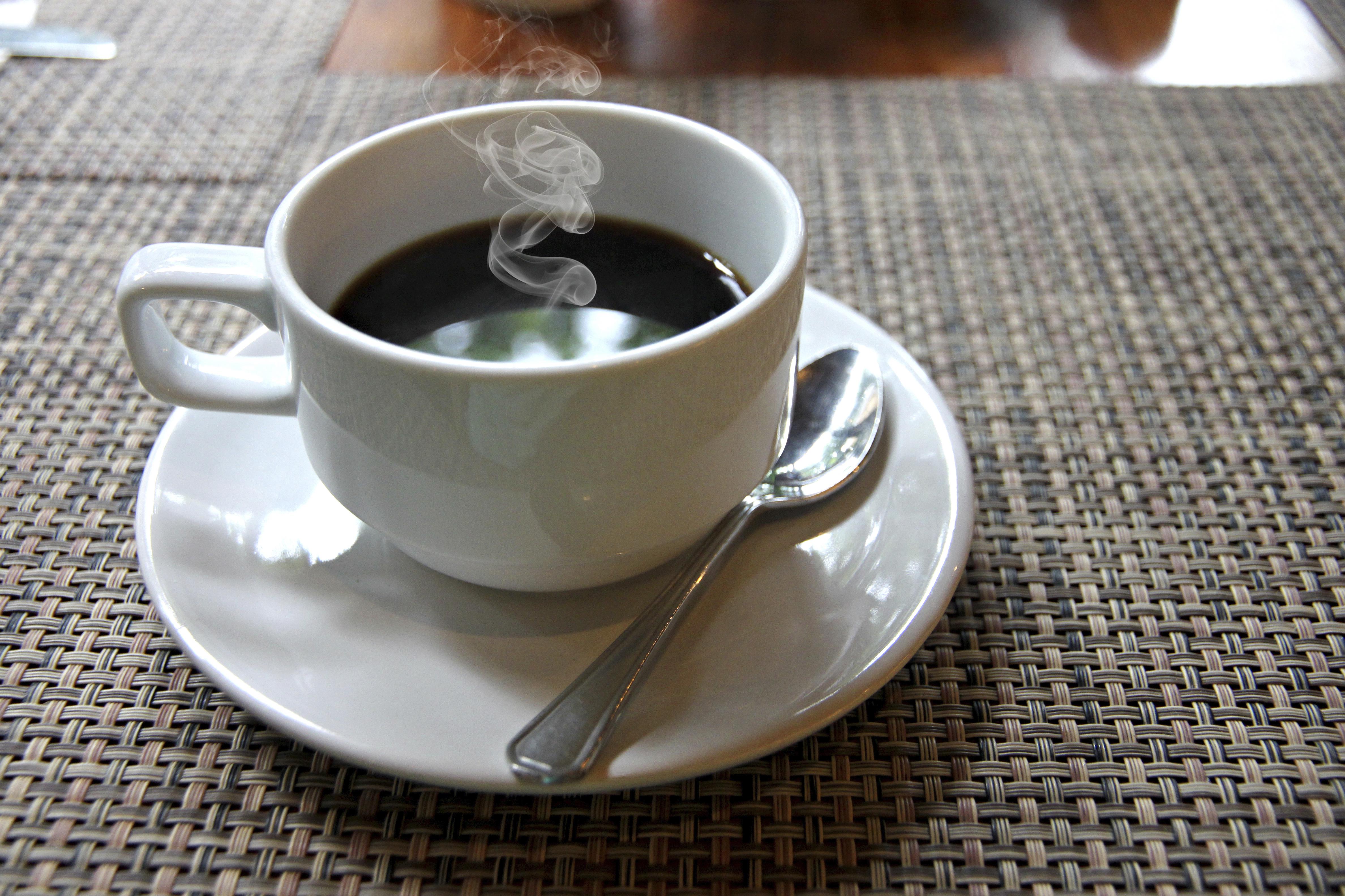 The Closeup hot Black coffee in a white cup on the table and have smoke coming out.
