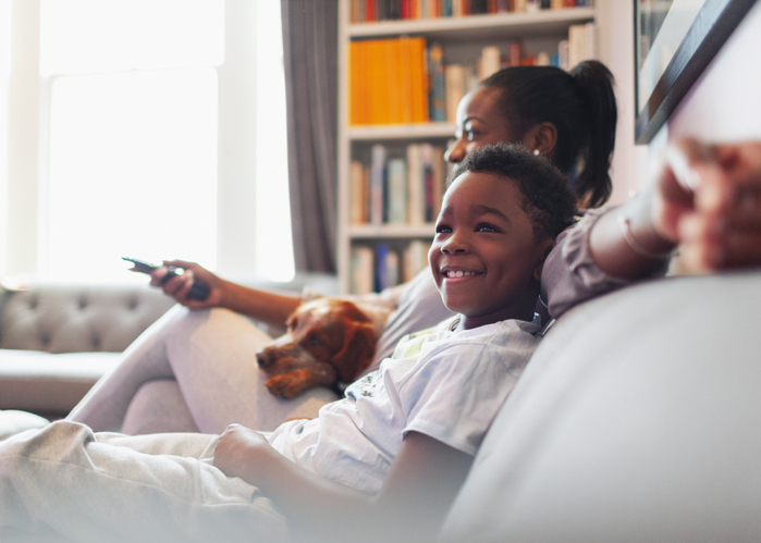 Happy boy watching TV with mother and dog on living room sofa