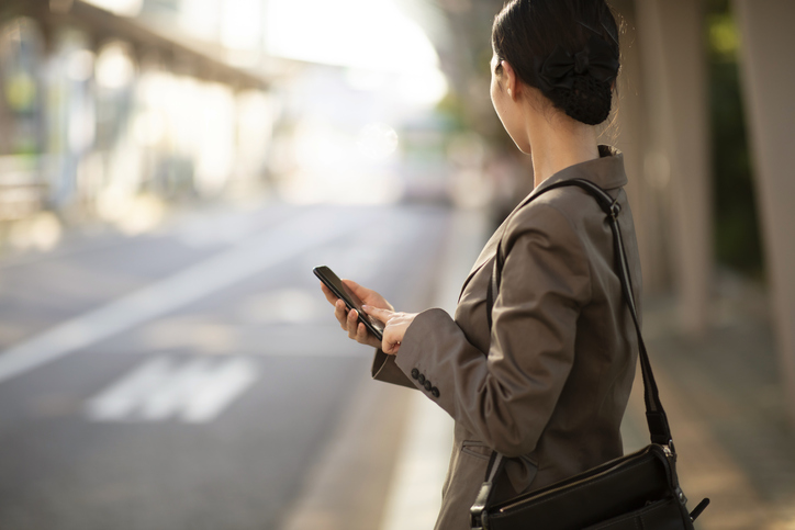 Businesswoman waiting on bus stop with smartphone