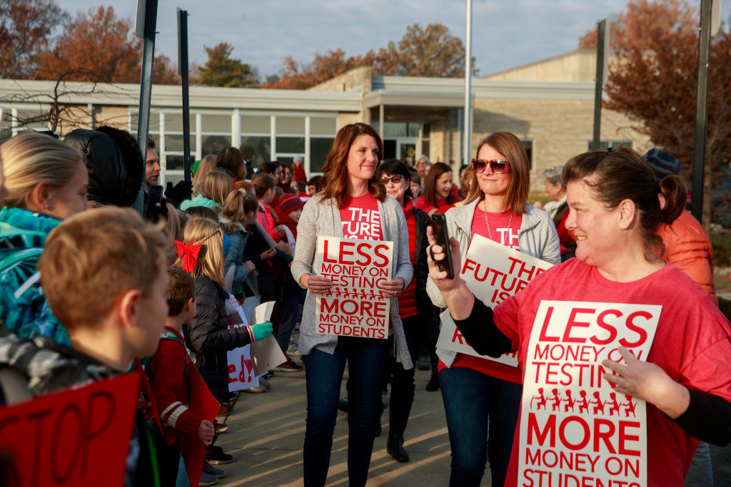 Teachers and elementary school students hold placards...
