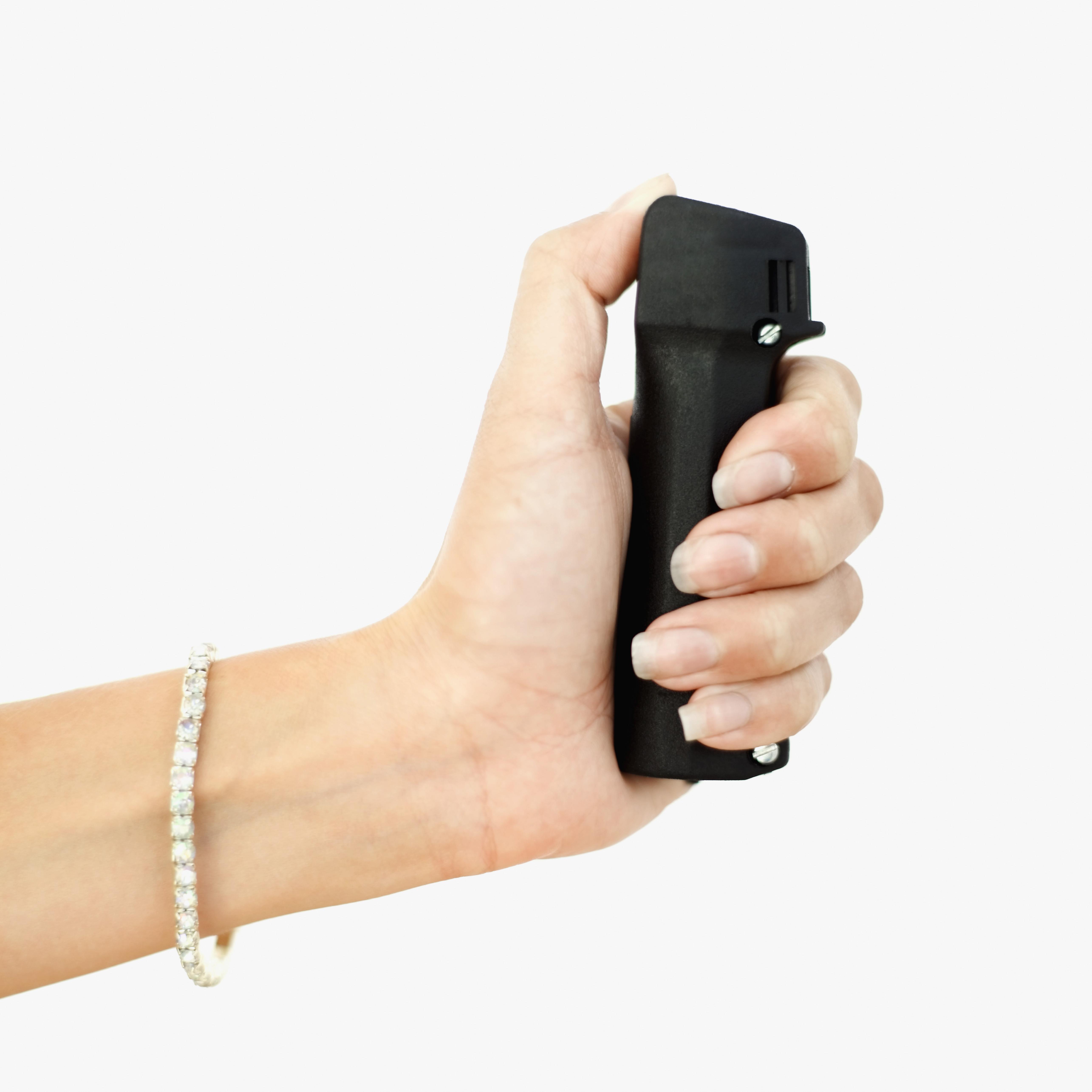 Close-up of a woman's hand wearing a solitaire diamond bracelet holding a pepper spray
