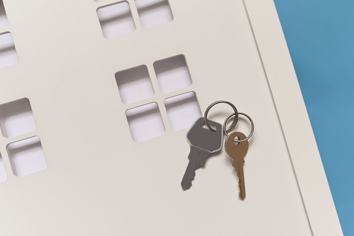 A toy wooden white house on a blue background, on the house are metal keys. The concept of a real estate purchase offer. Copy the space. Mortgages, affordable housing.