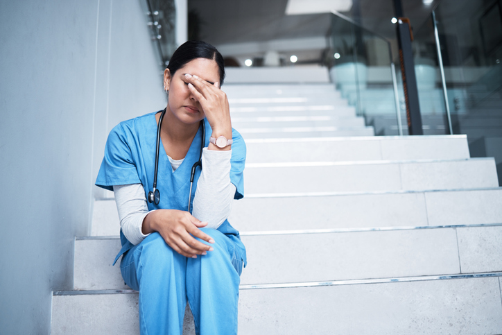 Shot of a female nurse looking stressed while sitting on a staircase