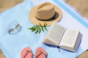 Beach towel with book, straw hat, sunglasses and flip flops on sand