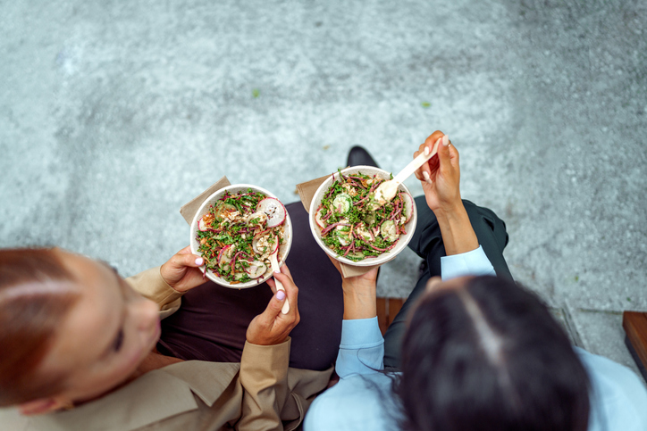 Two businesswomen eating salad during lunch break outdoors