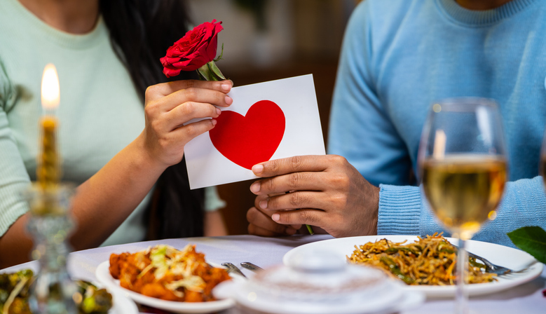 Close up shot of boyfriend giving rose greeting to girlfriend during candlelight dinner at home - concept of valentines day, relationship and romantic night