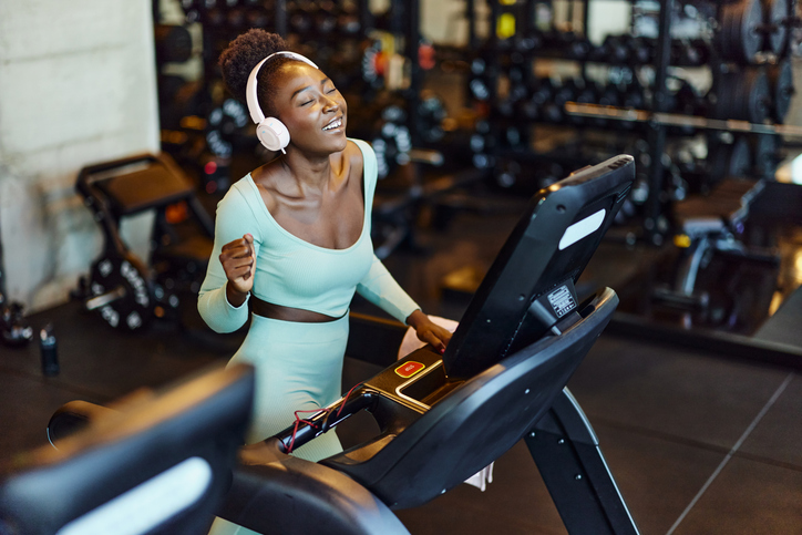 Happy black sportswoman enjoying in music on treadmill in a gym.